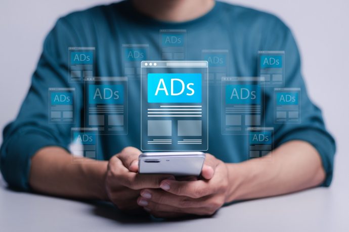 Digital marketing and online advertising to targeted customers. Shooting ads on cross feeds to optimize customer engagement. Person using mobile smartphone with virtual screen of ADs on website.